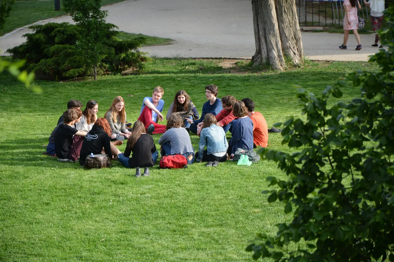 A big group of friends sitting in a circle on a park lawn