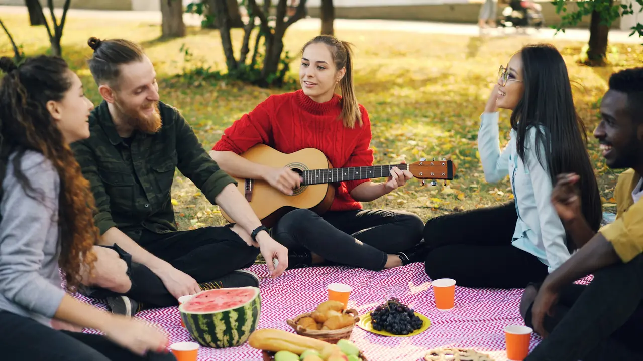 Friends playing guitar and sharing food on a picnic blanket