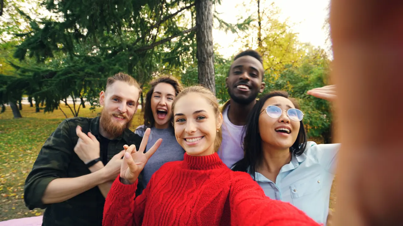 Five friends crowding into a smiling selfie in the park